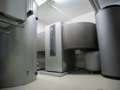 Modern heat pump water heater installed in a clean utility room with white walls.